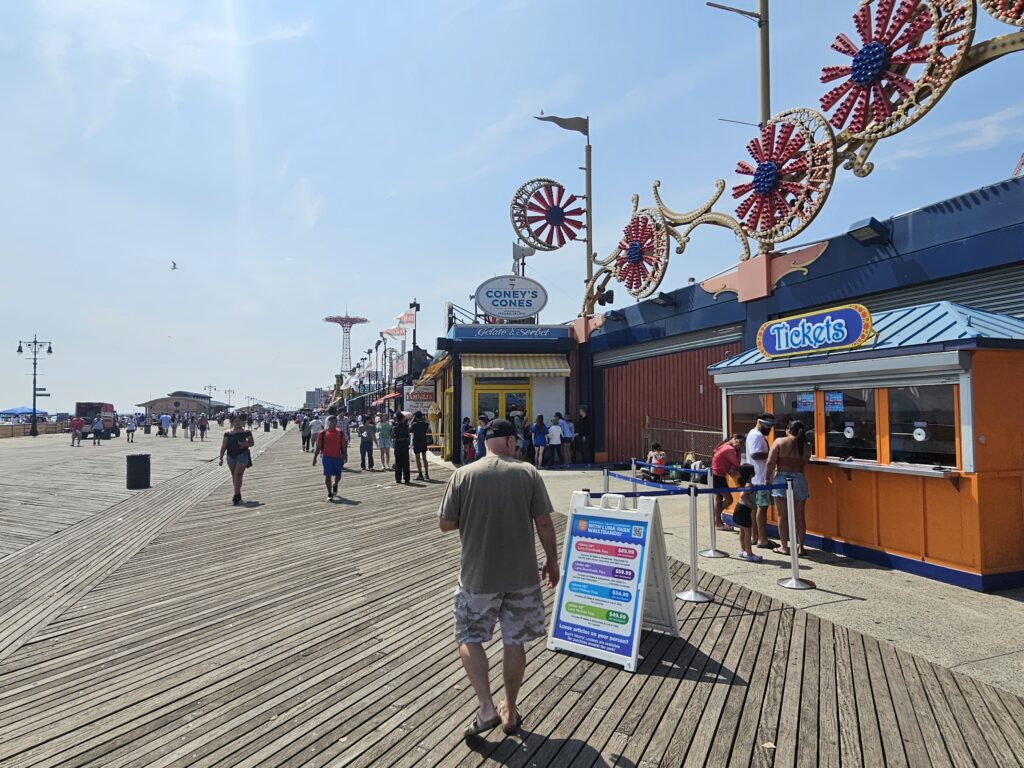 : Visitors walking along the Riegelmann Boardwalk past a game booth