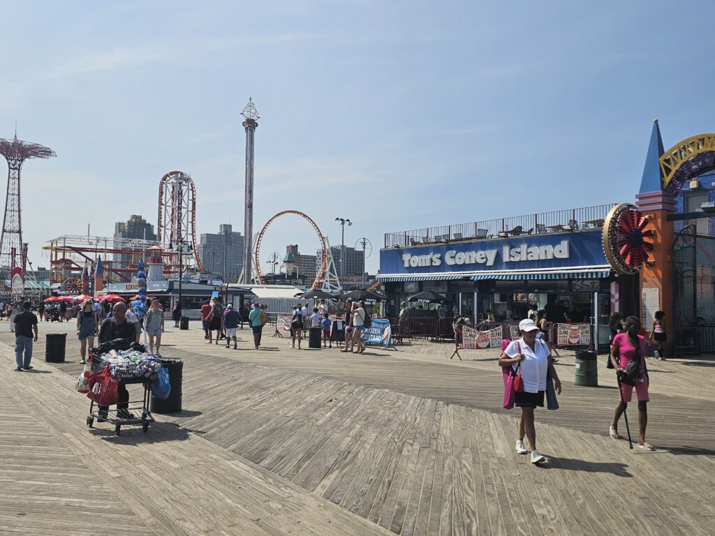 Boardwalk view of Luna Park rides with Tom's Coney Island sign