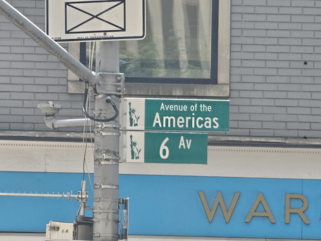 small/caption size — caption: "Avenue of the Americas (6th Avenue) street sign near the venue