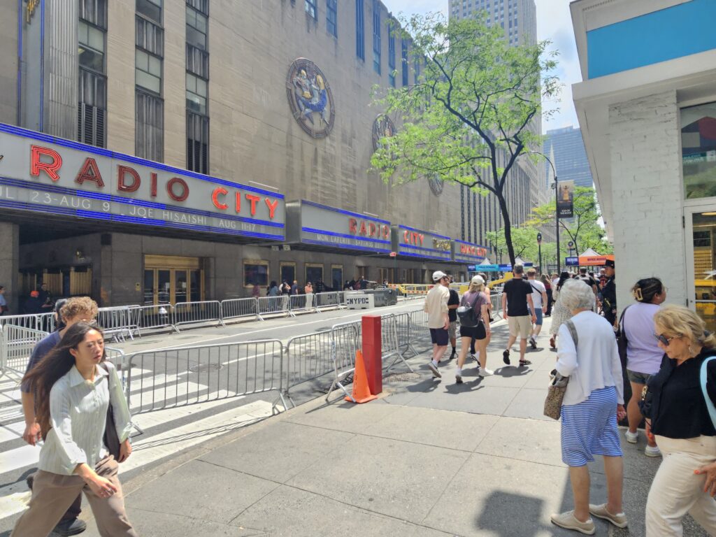 Sidewalk view of Radio City Music Hall with pedestrians walking past the marquee