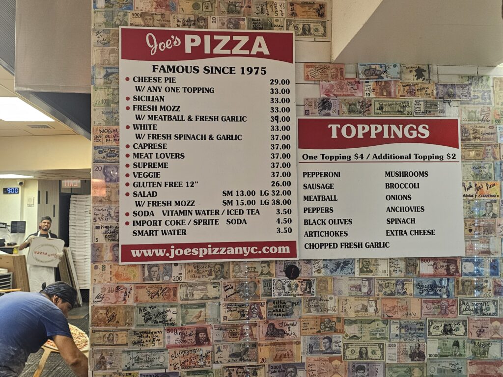 Joe's Pizza menu board with prices for pies, salads, and toppings