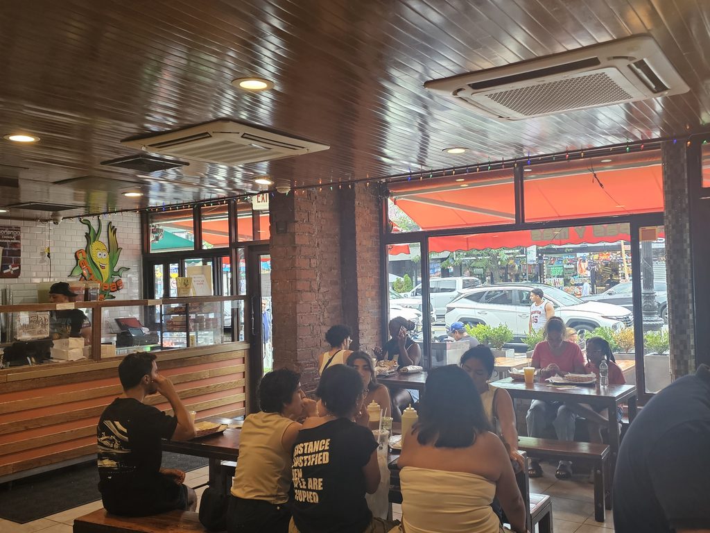Dining area at Cachapas y Mas NYC with customers seated near the orange storefront awning