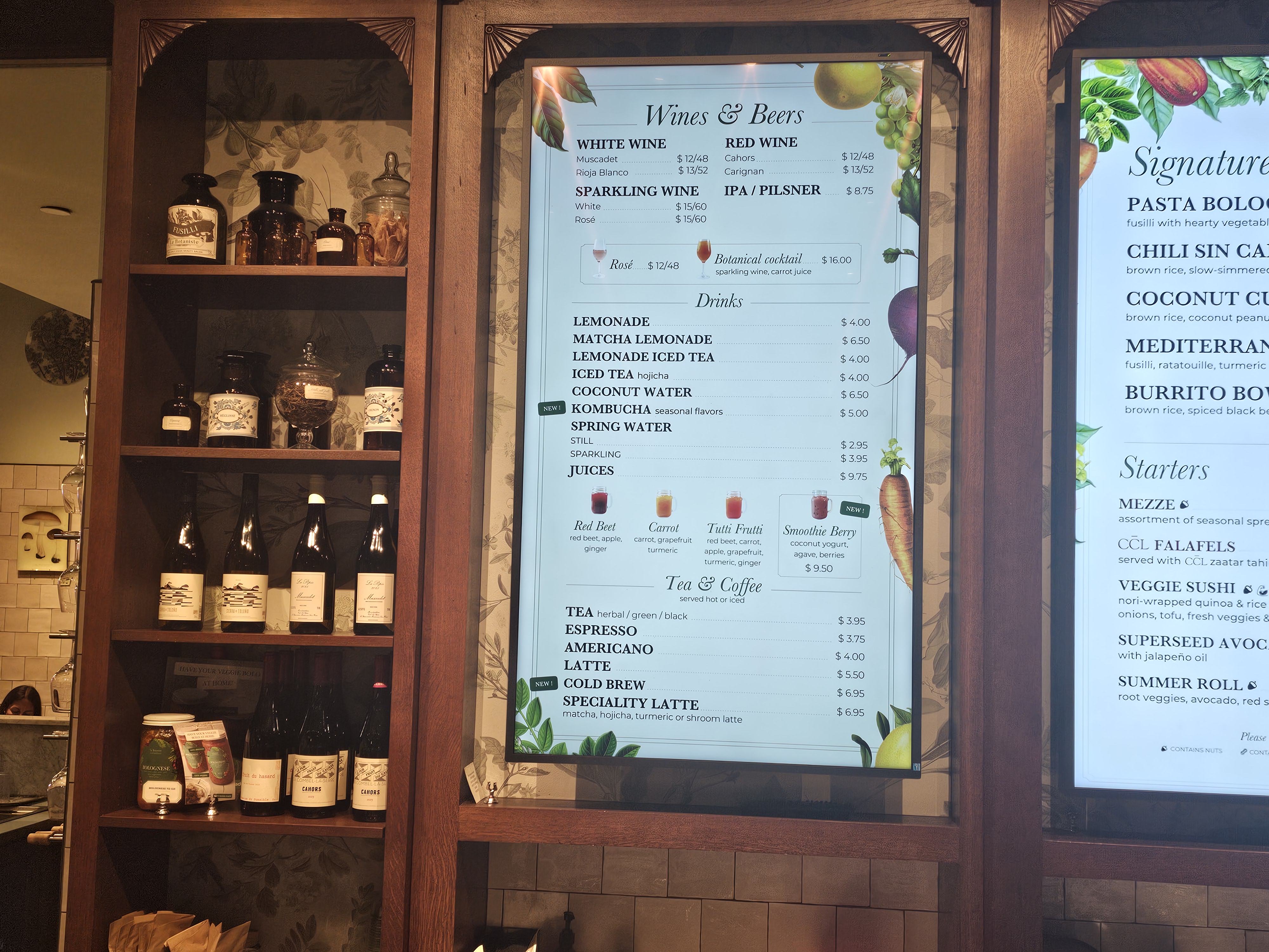 Drinks and natural wine menu board next to apothecary bottle shelving at Le Botaniste Bryant Park