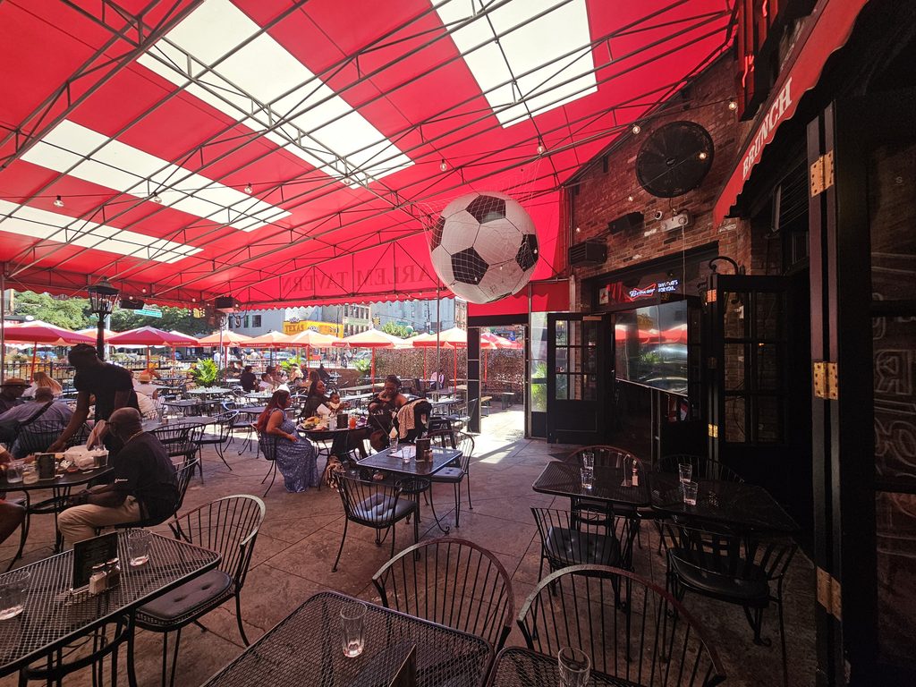 Covered outdoor beer garden seating with a hanging soccer ball decoration at Harlem Tavern NYC