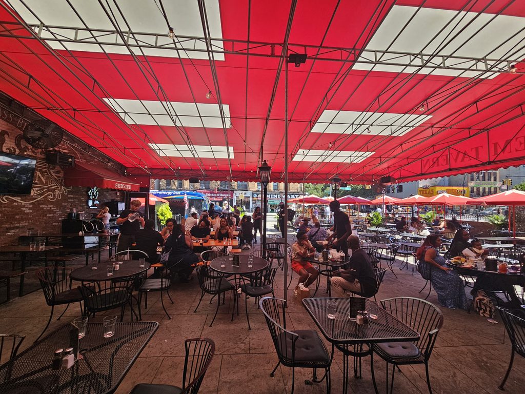 Open-air patio at Harlem Tavern NYC with orange picnic tables and a view of the Harlem street