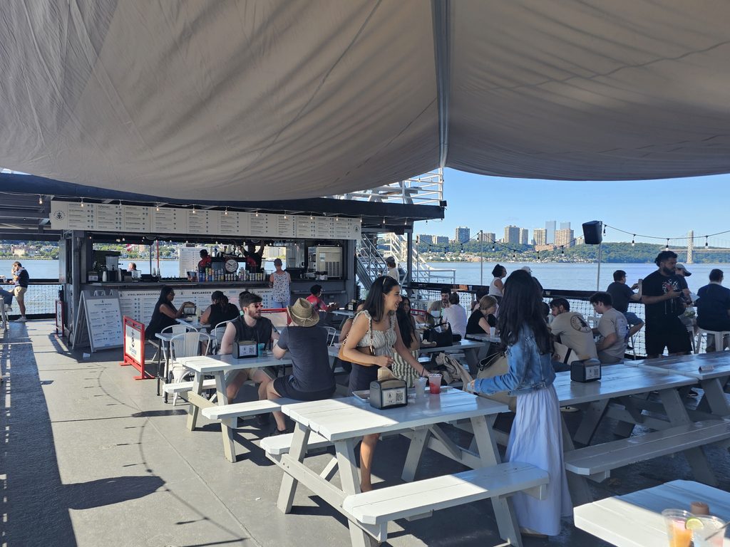 Guests dining on the deck of Baylander Steel Beach with the Hudson River and New Jersey skyline in view