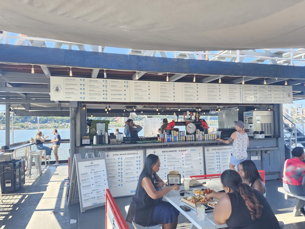 Shipping-container bar and kitchen with menu boards aboard Baylander Steel Beach