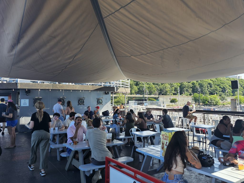 Crowd of guests seated at picnic tables on the deck of Baylander Steel Beach with the Palisades in the background