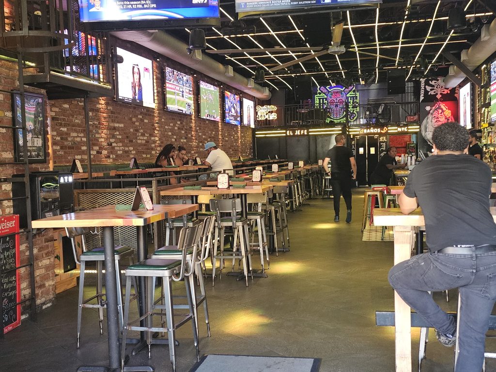 Brick-walled dining area at El Jefe Sports Cantina with neon signage and sports on TV