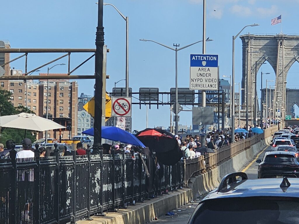 Crowds walking the wooden promenade on the Brooklyn Bridge past souvenir vendors