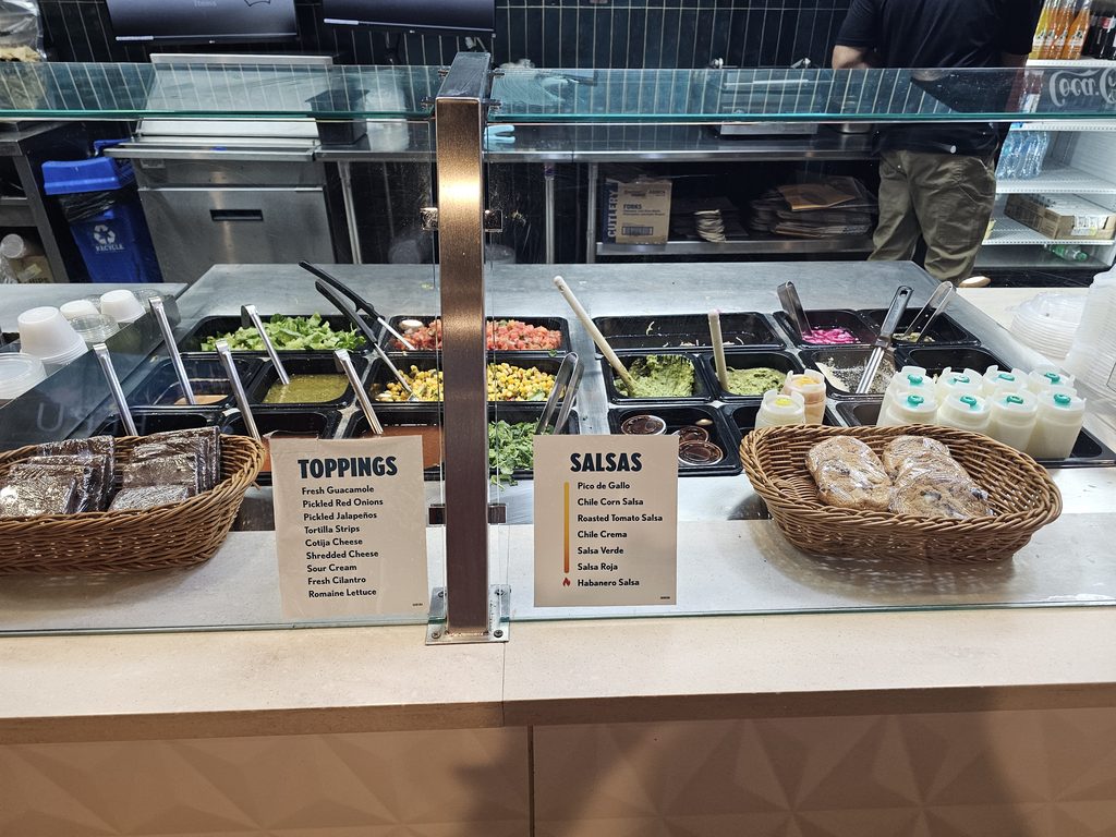 Toppings and salsas station at QDOBA Fordham Road for build-your-own burritos and bowls
